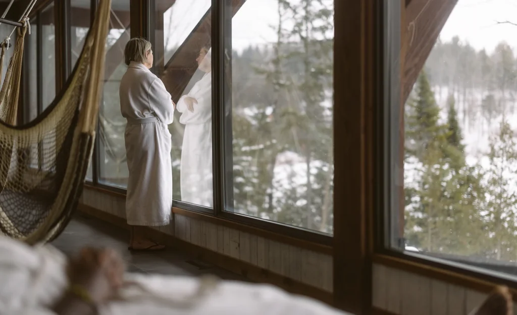 Femme en peignoir regardant forêt enneigée par fenêtre